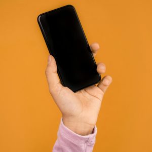 Close-up of a hand holding a smartphone against a bright orange backdrop, emphasizing modern technology.