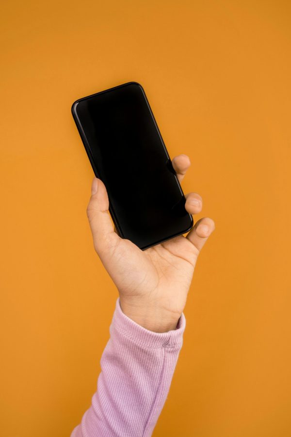 Close-up of a hand holding a smartphone against a bright orange backdrop, emphasizing modern technology.